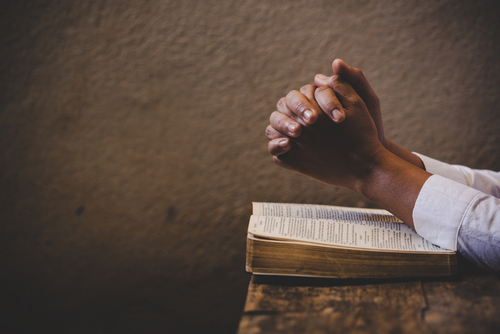 Hands,Folded,In,Prayer,On,A,Holy,Bible,In,Church