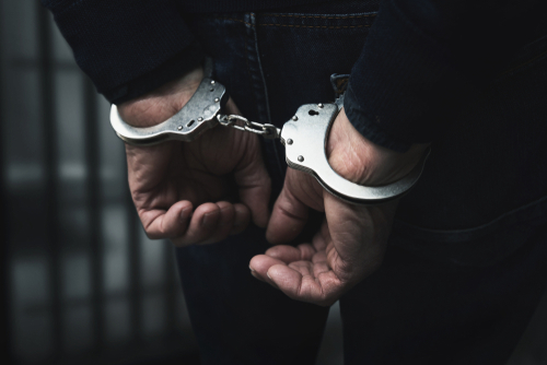 Arrested,Man,With,Cuffed,Hands,Behind,Prison,Bars